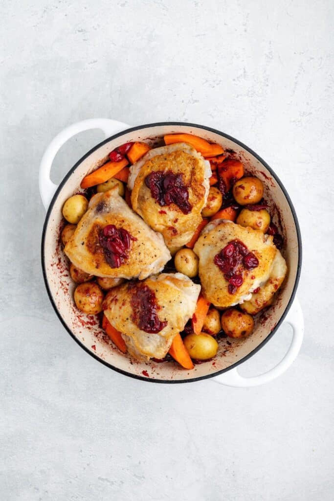 Roasted chicken thighs, cranberries, potatoes, and carrots in a white Dutch oven.