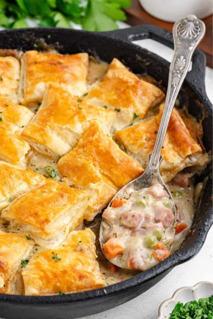 Creamy ham pot pie with puff pastry in a cast iron skillet and a silver spoon.