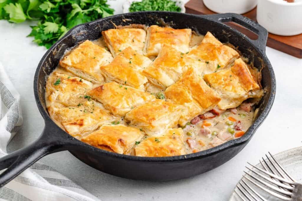 Leftover ham pot pie with a puff pastry crust in a black cast iron skillet.