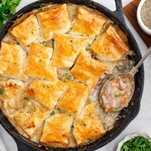Leftover ham pot pie in a cast iron skillet with square puff pastry crusts and a spoonful removed.