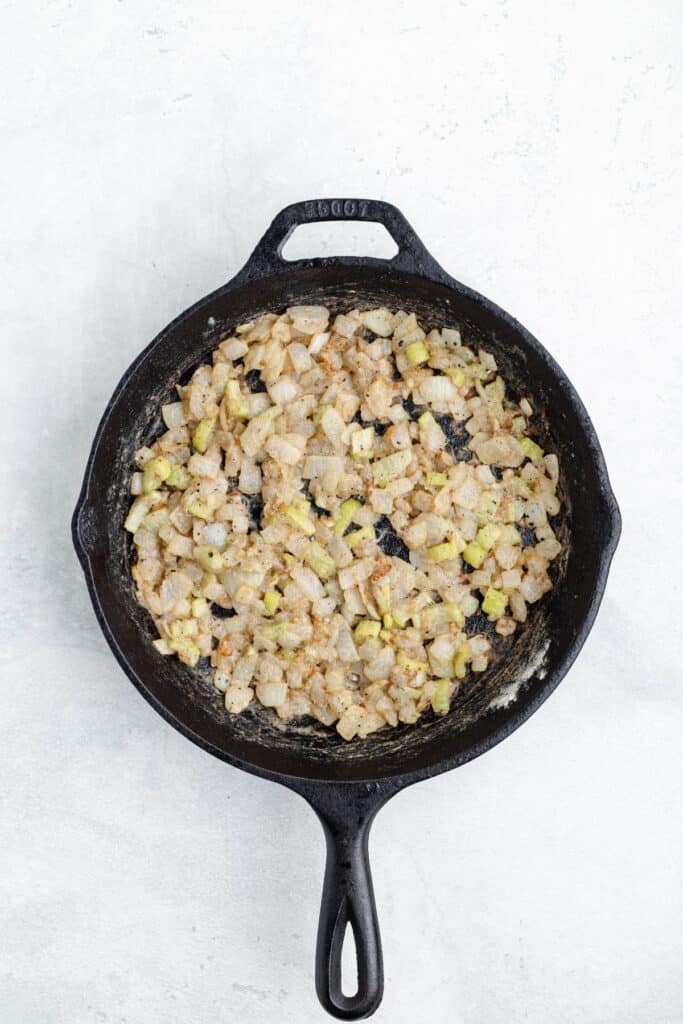 Diced onions and celery sautéing in a cast iron skillet.