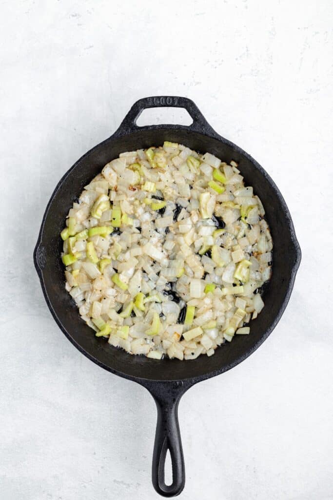 Diced onions and celery sautéing in a black cast iron skillet.