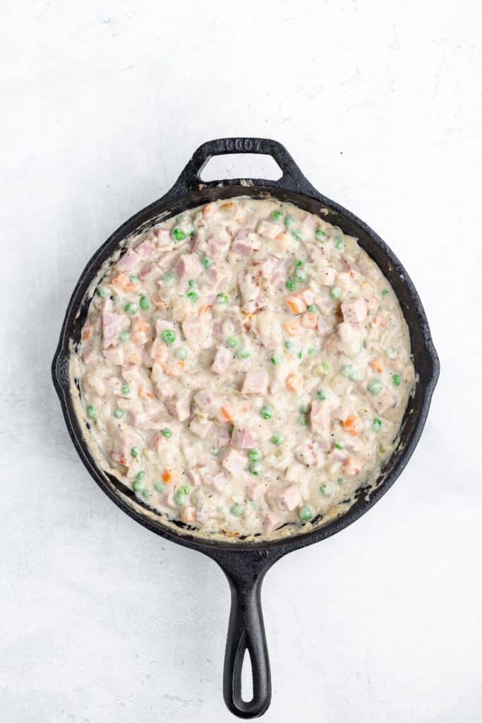 Creamy ham and vegetable filling served in a cast iron skillet.