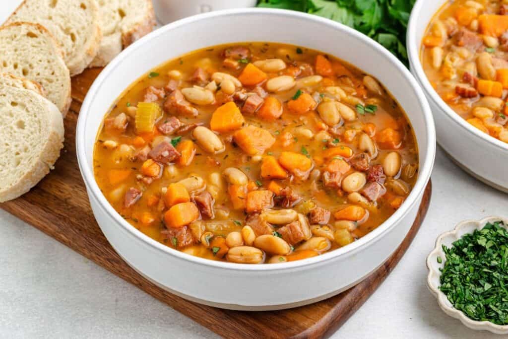 Two bowls of leftover ham and bean soup, served with sliced bread and chopped herbs.