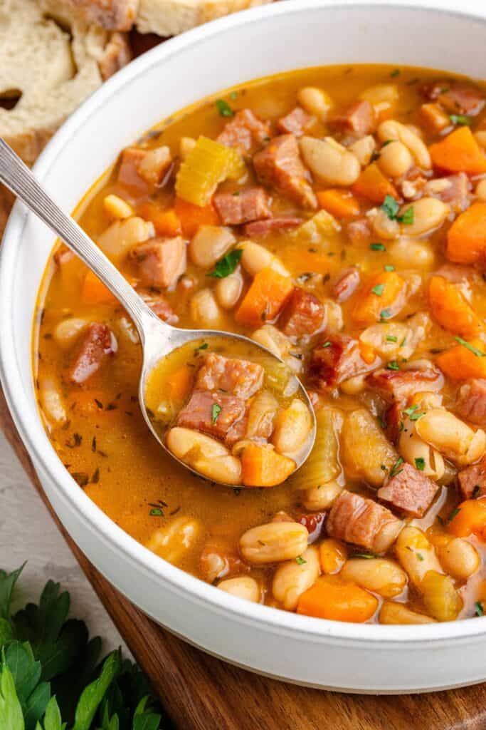 A spoonful of white bean and ham soup with carrots and celery in a white bowl.