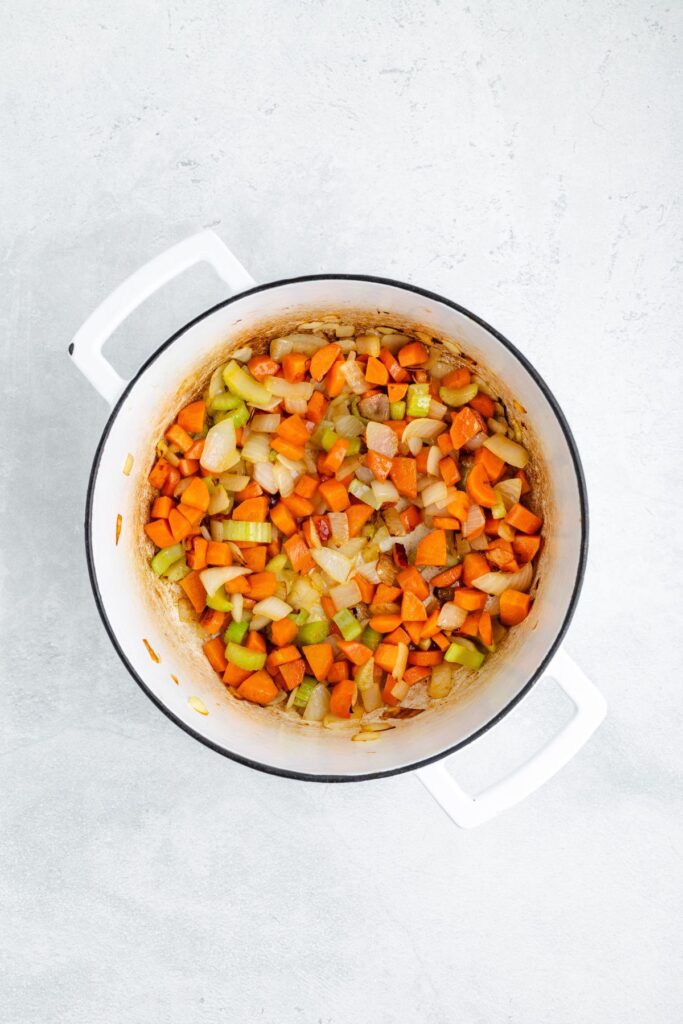 Diced carrots, celery, and onions sautéing in a white enameled cast iron pot.