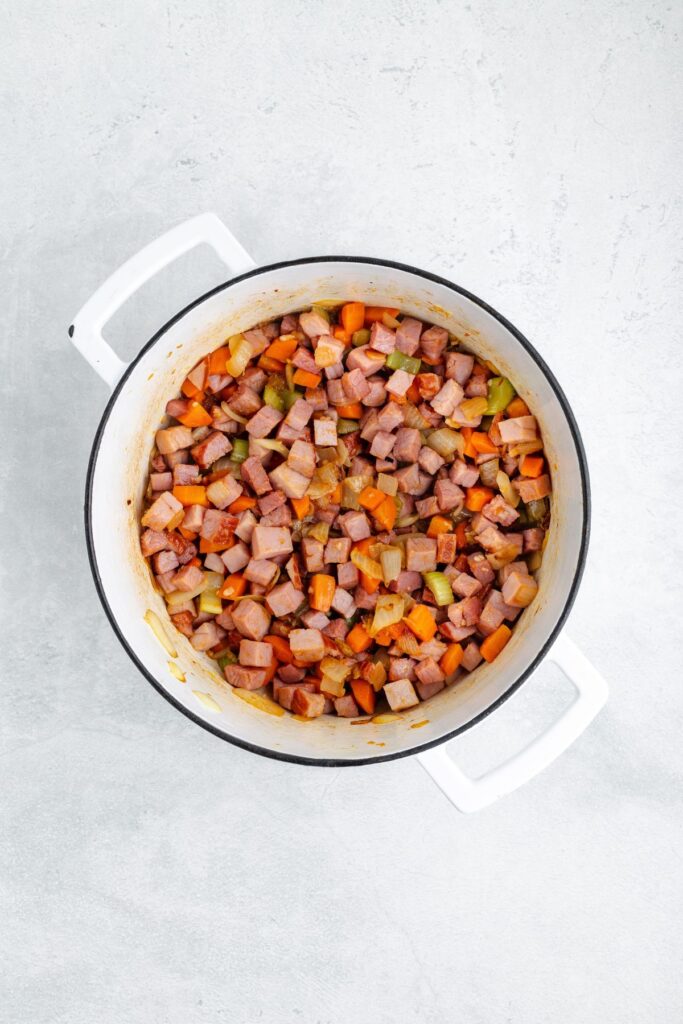Diced ham, carrots, celery, and onions sautéing in a white Dutch oven.