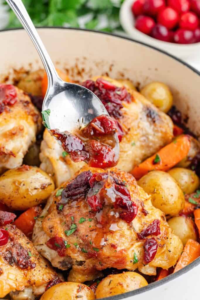 Cranberry glaze being drizzled over roasted chicken thighs, potatoes, and carrots.
