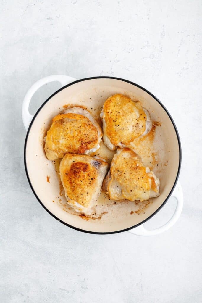 Four pan-seared chicken thighs in a white enameled cast iron pot.